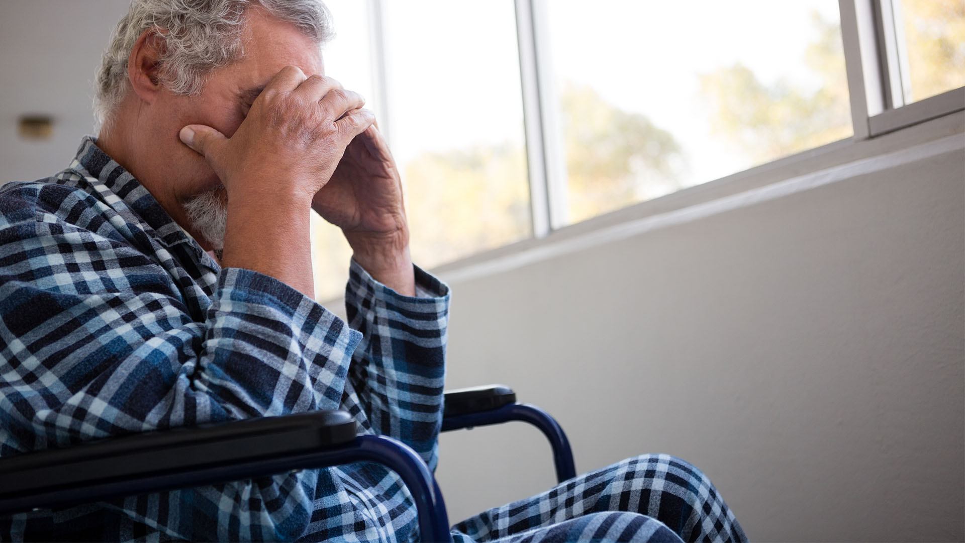 sad man in wheelchair with hands covering face